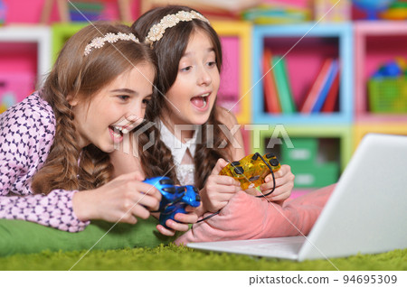 Portrait of two girls playing with joystick and laptop 94695309