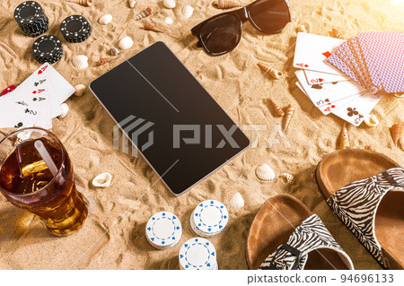 Online poker game on the beach with digital tablet and stacks of chips. Top view 94696133