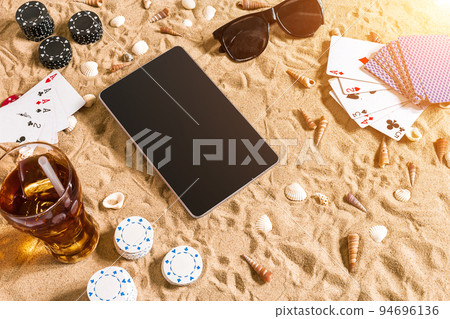 Online poker game on the beach with digital tablet and stacks of chips. Top view 94696136
