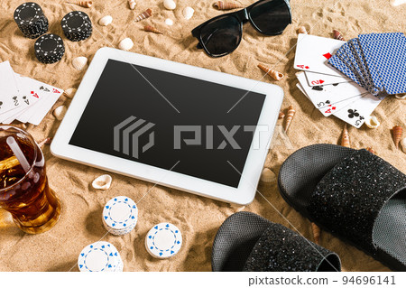 Online poker game on the beach with digital tablet and stacks of chips. Top view 94696141