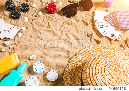 Beachpoker. Chips and cards on the sand. Around the seashells, sunglasses and hat. Top view Beachpoker. Chips and cards on the sand. Around the seashells, sunglasses and hat. Top view 94696158