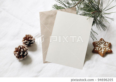 Christmas still life. Empty greeting card, invitation mockup. Gingerbread cookie, pine cones and pine tree branches on white linen tablecloth in sunlight. Gift wrapping concept. Winter festive flatlay 94696205