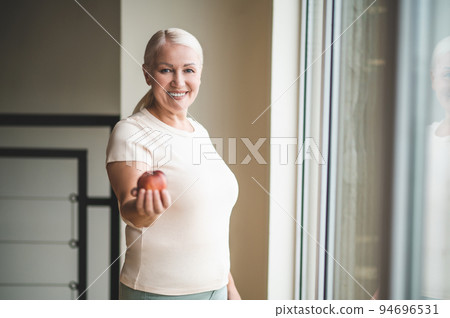 Pleased blonde lady demonstrating healthy fruit before the camera 94696531