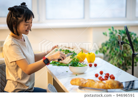Smiling young housewife cooking in front of the smartphone camera 94696591
