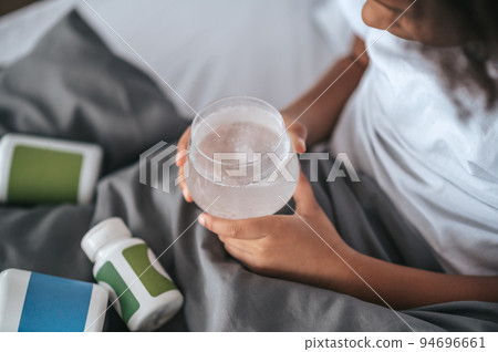 A girl taking a pill while lying in bed and feeling unwell 94696661