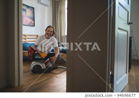 Man sitting on the floor and gathering the vacuum cleaner Man sitting on the floor and gathering the vacuum cleaner 94696677