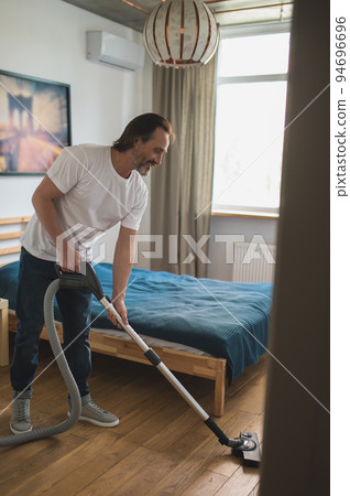 Man in white tshirt doing vacuum cleaning and looking involved Man in white tshirt doing vacuum cleaning and looking involved 94696696