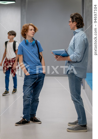 Pupil having a conversation with his schoolteacher in the corridor 94697384