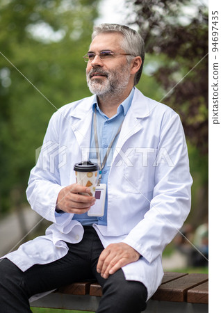 Bearded mature man in na lab coat with a cup of coffee Bearded mature man in na lab coat with a cup of coffee 94697435