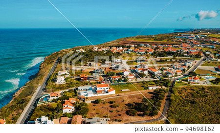 Beautiful natural landscape. Portugal.  Drone view of a beautiful European city with a hilly landscape on ocean background. Aerial view of a small European town against blue sky and Atlantic Ocean. 94698162