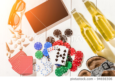 Card deck surrounded by poker chips and scattered seashells on white wooden background with copy space Card deck surrounded by poker chips and scattered seashells on white wooden background with copy space 94698306