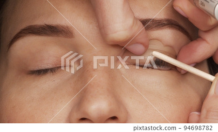 Woman on modern eyelash lamination procedure in a professional beauty salon. Master applies special glue before the eyelash curling procedure, close up. Beauty salon.. Woman on modern eyelash lamination procedure in a professional beauty salon. Master applies special glue before the eyelash curling procedure, close up. Beauty salon.. 94698782