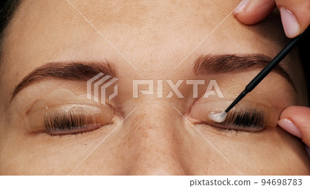 Woman on modern eyelash lamination procedure in a professional beauty salon. Master applies special glue before the eyelash curling procedure, close up. Beauty salon.. 94698783