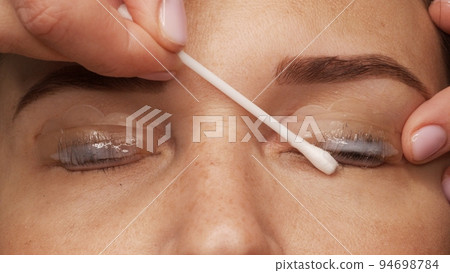 Woman face on modern eyelash lamination procedure in a professional beauty salon. Master applies special glue before the eyelash curling procedure, close up. Beauty salon.. Woman face on modern eyelash lamination procedure in a professional beauty salon. Master applies special glue before the eyelash curling procedure, close up. Beauty salon.. 94698784