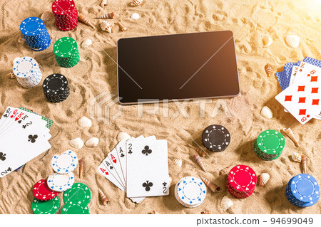 Online poker game on the beach with digital tablet and stacks of chips. Top view 94699049