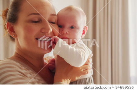 Young happy  mother  holds her newborn baby, window with sunset behind on a background. Closeup portrait of a loving mother with a child. Happy mom with her  infant son. Mum loves of her infant child 94699556