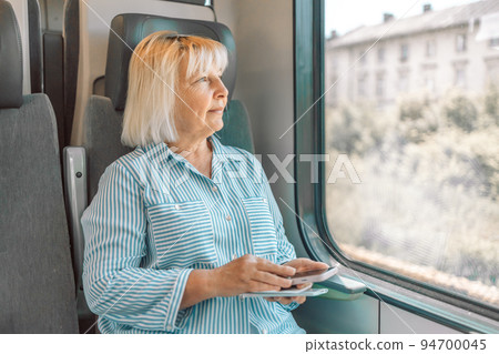 Happy Caucasian senior woman using transport application on smartphone while travelling by high speed train 94700045