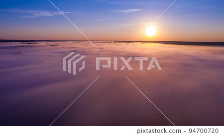 Aerial  view of a beautiful summer  landscape with a fog while dawn.  Photo from drone of a foggy landscape in spring. Top view to land while sunrise. Sun is above the horizon 94700720