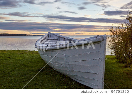Wooden white boat on the shore of the bay of the lake against the backdrop of clouds and the setting sun 94701230