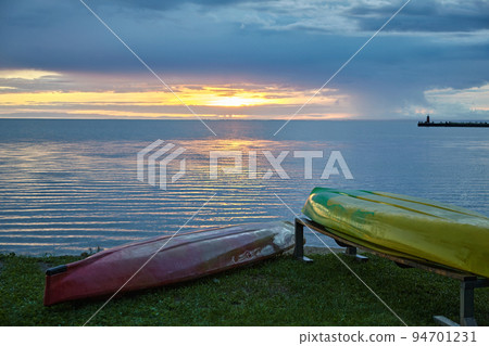 Canoe boats on the shore of the bay bay lake against the backdrop of the setting sun 94701231