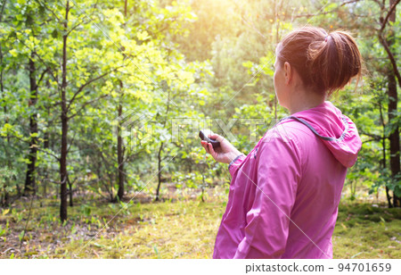 A girl in a pink sweater uses a navigator in the forest to determine her location. Mushroom picker and compass. Wandering through the forest. Copy space for text A girl in a pink sweater uses a navigator in the forest to determine her location. Mushroom picker and compass. Wandering through the forest. Copy space for text 94701659