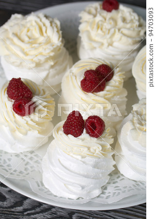 Cake Anna Pavlova, meringue and cream. Garnished with raspberries. Lying on a platter, close-up. 94703093