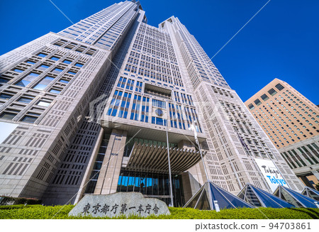 Tokyo cityscape in Japan Tokyo Metropolitan Government Building. A view of the Tokyo Metropolitan Government No. 1 Main Building and the stone marker in front of the entrance, bathed in the strong morning sun. 94703861
