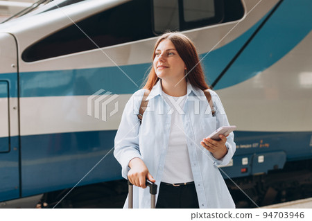 Young redhhead woman waiting train with backpack and using smart phone. Railroad transport concept, Traveler.Woman with suitcase walking at railroad station platform. Travel to vacation by train Young redhhead woman waiting train with backpack and using smart phone. Railroad transport concept, Traveler.Woman with suitcase walking at railroad station platform. Travel to vacation by train 94703946