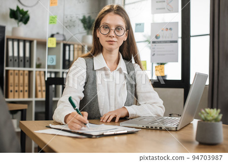 Attractive blond businesswoman in white shirt sitting at desk with papers and wireless laptop Attractive blond businesswoman in white shirt sitting at desk with papers and wireless laptop 94703987