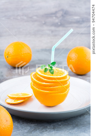 Fresh orange slices in a stack, mint leaves and a straw for a drink. Simulated orange juice. Vertical view Fresh orange slices in a stack, mint leaves and a straw for a drink. Simulated orange juice. Vertical view 94704474