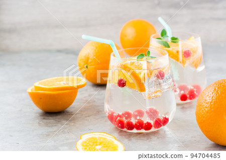 Hard seltzer cocktail with orange, cranberry and mint in glasses and cut oranges on the table. Alcoholic highly carbonated drink 94704485