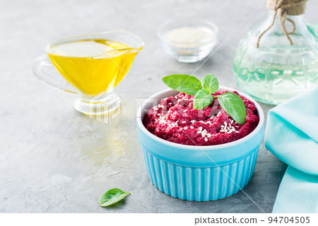 Baked beet hummus in a bowl with sesame seeds and basil on the table. Close-up Baked beet hummus in a bowl with sesame seeds and basil on the table. Close-up 94704505