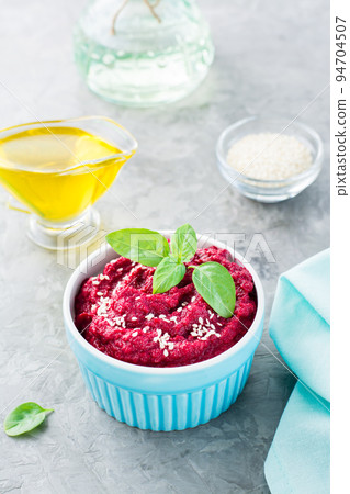 Baked beet hummus in a bowl with sesame seeds and basil on the table. Vertical view Baked beet hummus in a bowl with sesame seeds and basil on the table. Vertical view 94704507