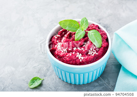 Homemade baked beetroot hummus in a bowl with sesame seeds and basil on the table. Close-up Homemade baked beetroot hummus in a bowl with sesame seeds and basil on the table. Close-up 94704508