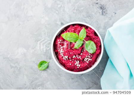 Homemade baked beetroot hummus in a bowl with sesame seeds and basil on the table. Close-up. Top view 94704509