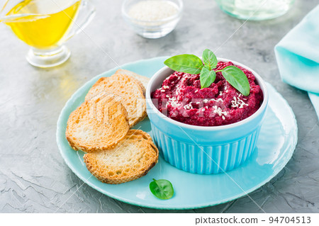 Homemade baked beetroot hummus in a bowl with sesame seeds and basil and baked small toast on a plate on the table Homemade baked beetroot hummus in a bowl with sesame seeds and basil and baked small toast on a plate on the table 94704513