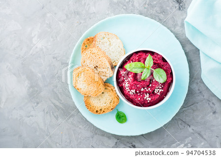 Homemade baked beetroot hummus in a bowl with sesame seeds and basil and baked small toast on a plate on the table. Top view Homemade baked beetroot hummus in a bowl with sesame seeds and basil and baked small toast on a plate on the table. Top view 94704538