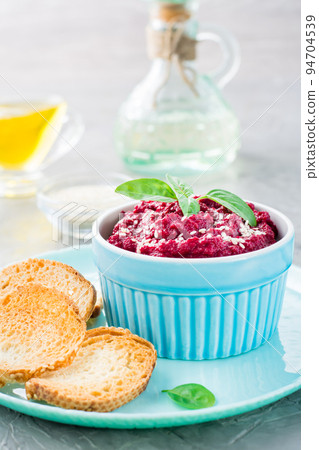 Homemade baked beetroot hummus in a bowl with sesame seeds and basil and baked small toast on a plate on the table. Vertical view Homemade baked beetroot hummus in a bowl with sesame seeds and basil and baked small toast on a plate on the table. Vertical view 94704539