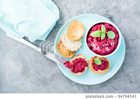 Homemade bruschetta with beetroot hummus on small toast on a plate and a table knife on the table. Top view Homemade bruschetta with beetroot hummus on small toast on a plate and a table knife on the table. Top view 94704541