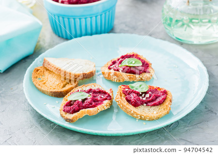 Homemade bruschetta with beetroot hummus on small baked baguette toast on a plate on the table Homemade bruschetta with beetroot hummus on small baked baguette toast on a plate on the table 94704542