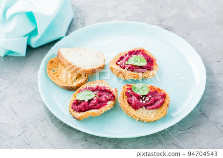 Homemade bruschetta with beetroot hummus on small baked baguette toast on a plate on the table. Close-up Homemade bruschetta with beetroot hummus on small baked baguette toast on a plate on the table. Close-up 94704543