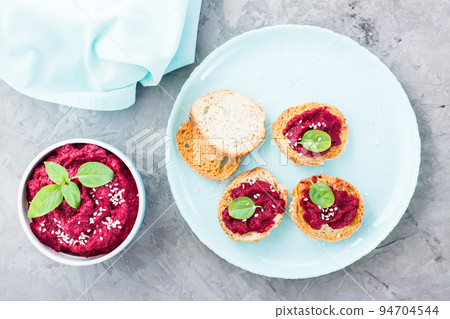 Homemade bruschetta with beetroot hummus on small baked baguette toast on a plate and a bowl of hummus on the table. Top view Homemade bruschetta with beetroot hummus on small baked baguette toast on a plate and a bowl of hummus on the table. Top view 94704544