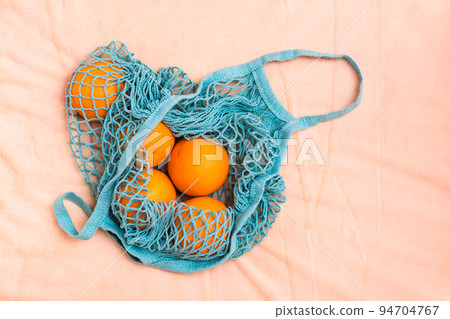 Fresh oranges in a mesh bag on a fabric background. Zero waste Fresh oranges in a mesh bag on a fabric background. Zero waste 94704767