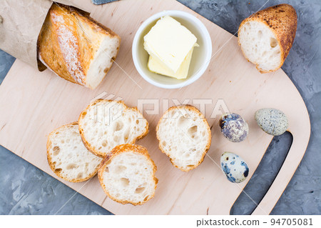 Cooking a hearty breakfast with fresh baguette, butter and quail eggs on a cutting board on a table. Top view. Close-up 94705081