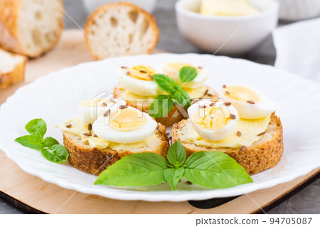 Hearty breakfast in the morning. Fresh baguette sandwiches with butter, quail eggs, flax seeds and basil seeds on a plate. Close-up Hearty breakfast in the morning. Fresh baguette sandwiches with butter, quail eggs, flax seeds and basil seeds on a plate. Close-up 94705087