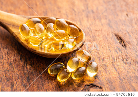 Fish oil capsules. Yellow omega 3 pills in spoon on wooden table. 94705616