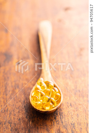 Fish oil capsules. Yellow omega 3 pills in spoon on wooden table. 94705617