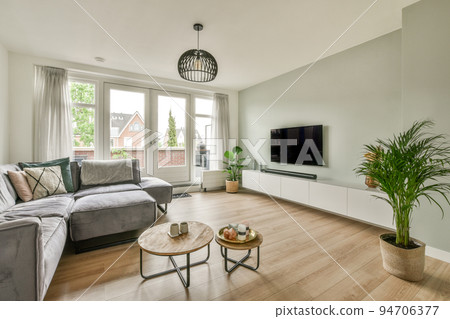 Comfortable sofas and wooden table placed near potted plants against window in living room of modern apartment with television Comfortable sofas and wooden table placed near potted plants against window in living room of modern apartment with television 94706377