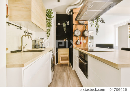 Fragment of interior of light narrow home kitchen with minimalist style white furniture with sink and stove Fragment of interior of light narrow home kitchen with minimalist style white furniture with sink and stove 94706426