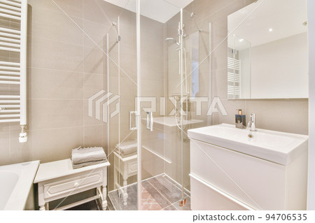Sinks with mirrors and clean bathtub located near shower box with glass door in modern bathroom with white tiled walls 94706535
